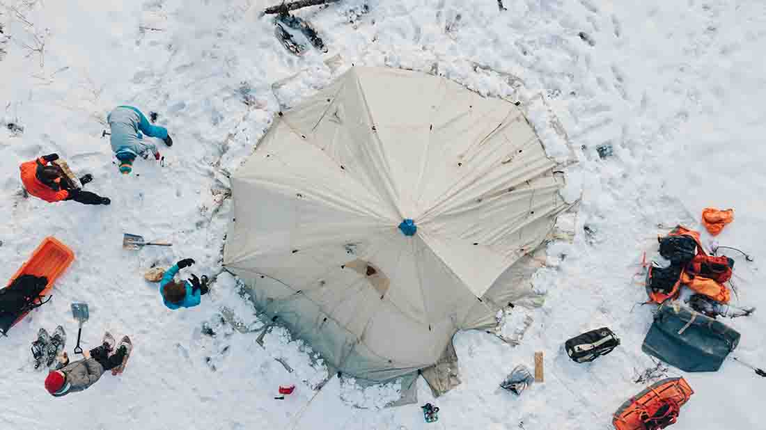 aerial image of the white tent in the snow with men all around it