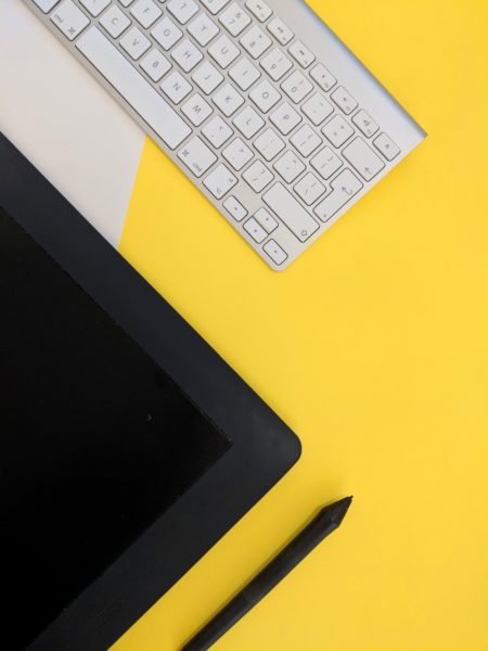 a black keyboard and a tablet with a stylus lying on a yellow desk