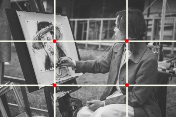 Photograph of a woman painting an image of a lady with a hat