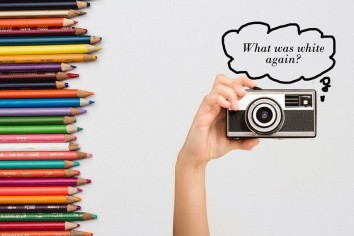 color pencils of various colors lying horizontally with a camera held by a hand