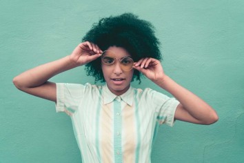 Girl holding her glasses in front of a green background