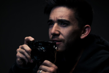 Man holding a small camera in his hand with a dark black background
