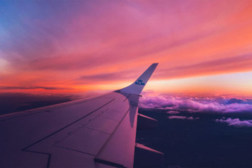 A plane wing flying through the clouds at dusk with warm colors all around